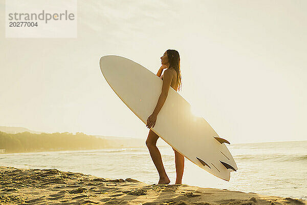 Junge Frau steht mit Surfbrett am Strand
