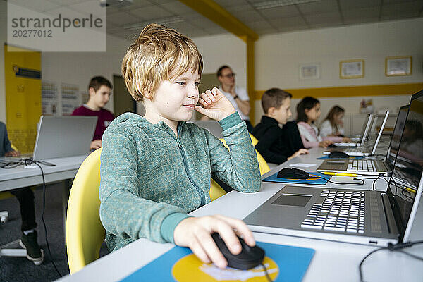 Blonder Junge lernt im Klassenzimmer Computerprogrammierung per Laptop