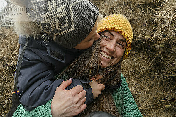 Playful boy embracing mother by haystack at farm