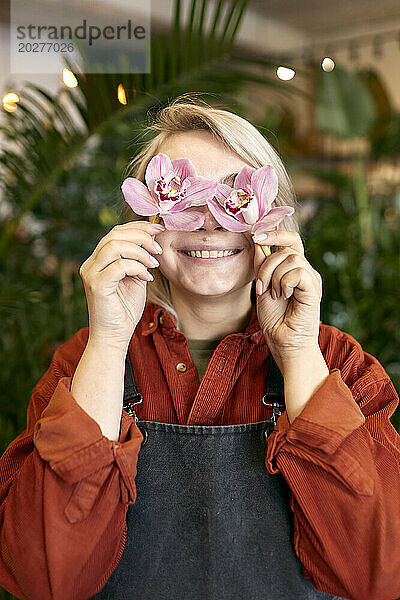 Lächelnder Florist hält rosafarbene Blumen über den Augen