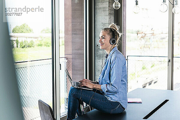 Lächelnde Geschäftsfrau sitzt am Schreibtisch mit Laptop im Büro