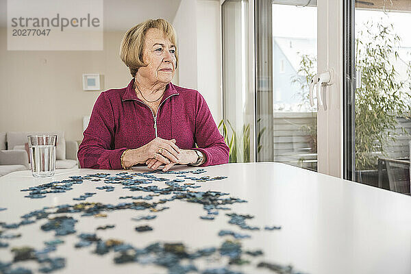 Nachdenkliche Frau sitzt mit Puzzle am Tisch