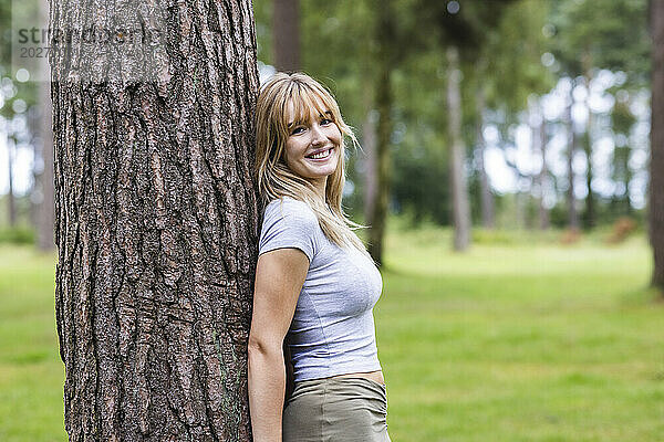 Glückliche junge schöne Frau lehnt an Baum im Wald