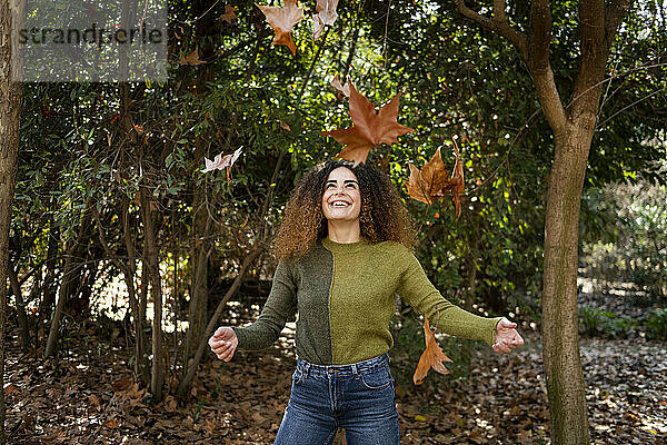 Verspielte Frau steht unter fallenden Blättern im Park