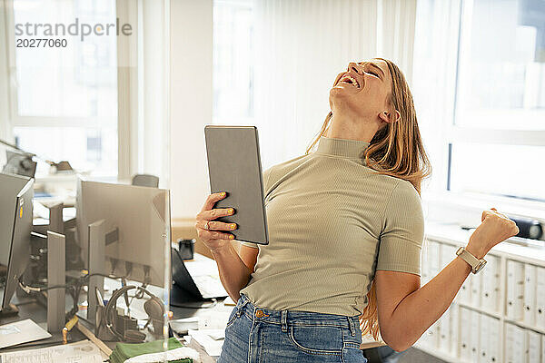 Aufgeregte Geschäftsfrau mit Tablet-PC feiert Erfolg im Büro