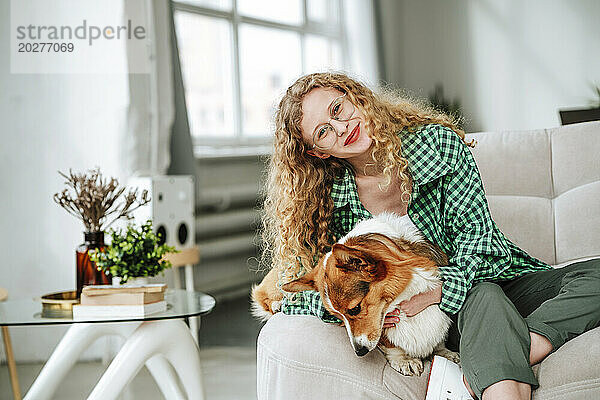 Lächelnde Frau sitzt mit Hund zu Hause