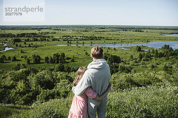 Vater und Tochter umarmen sich und schauen auf die Rasenfläche