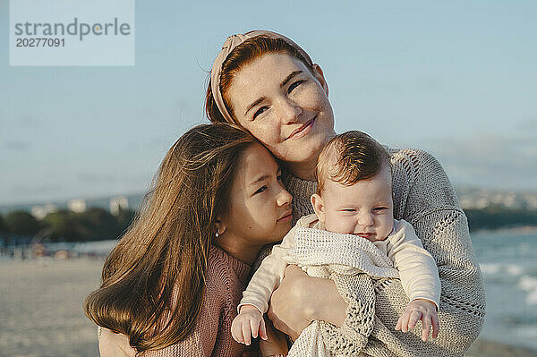 Lächelnde Mutter verbringt an einem sonnigen Tag ihre Freizeit mit ihren Töchtern am Strand