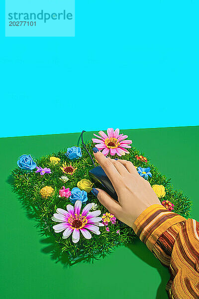 Hand einer Geschäftsfrau  die eine Computermaus auf Frühlingsblumen hält
