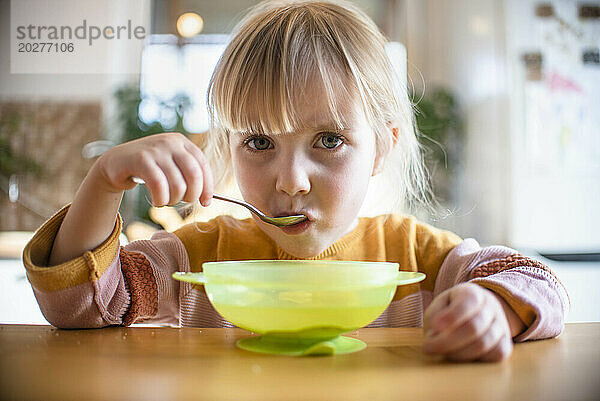 Nettes blondes Mädchen  das zu Hause Frühstück mit Löffel isst
