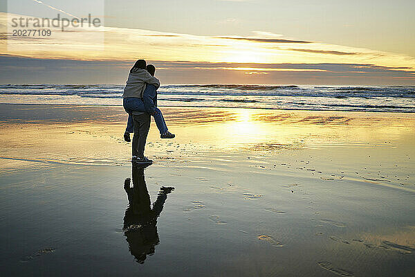 Junger Mann huckepack mit Freundin und spaziert am Strand am Meer
