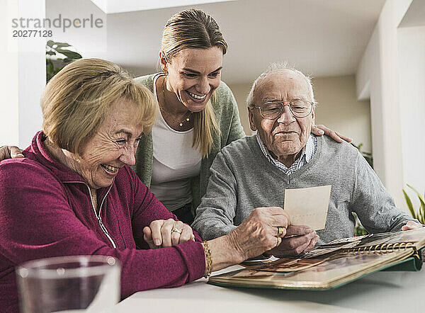 Glückliche häusliche Pflegekraft mit älterem Paar beim Betrachten von Fotos