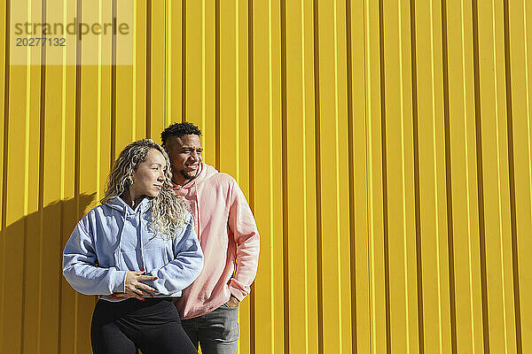 Junges Paar steht an einem sonnigen Tag vor einer gelben Wand