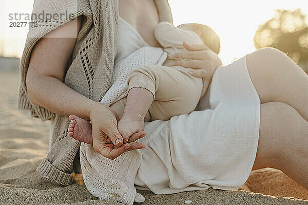 Woman sitting on sand and breastfeeding daughter at beach