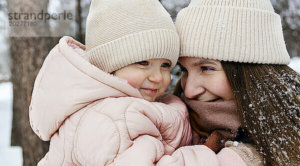 Smiling mother and daughter wearing knit hats at winter park