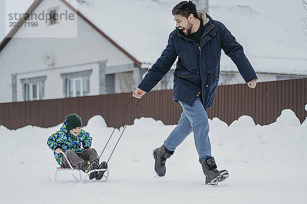 Father pulling son sitting on sled in winter