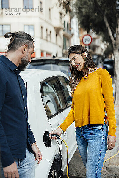 Lächelnde Frau spricht mit Mann und lädt Elektroauto auf