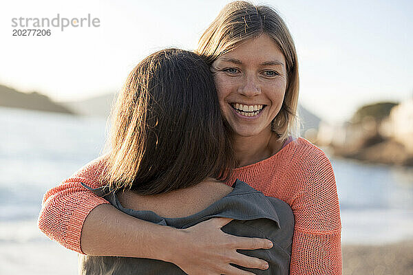 Glückliche Frau umarmt Freundin am Strand an einem sonnigen Tag