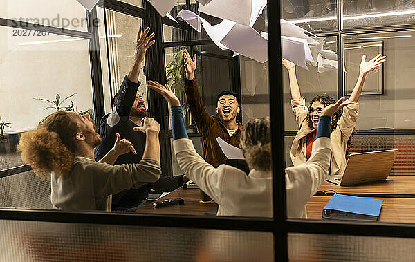 Fröhliche Geschäftskollegen werfen Papiere durch die Glasscheibe im Büro