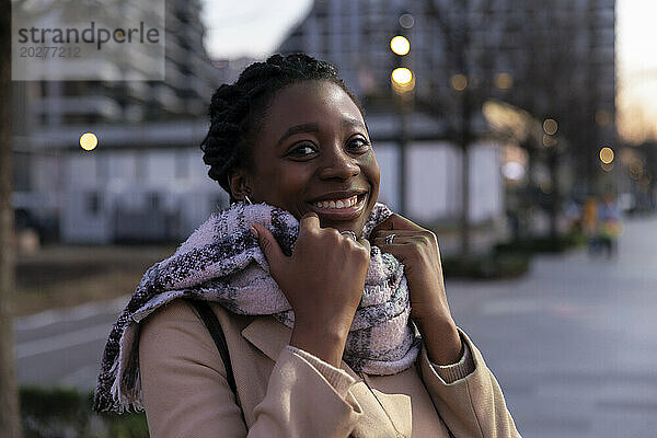 Happy woman wearing scarf in city at dusk