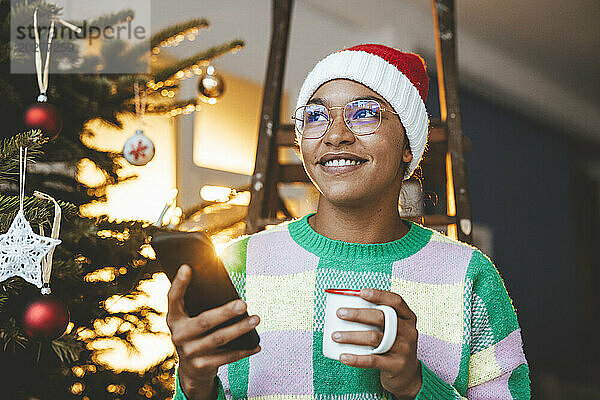 Nachdenkliche Frau mit Smartphone und Kaffeetasse zu Hause