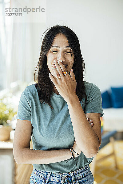 Happy woman with eyes closed covering mouth at home