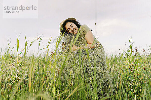 Lächelnde Frau umarmt Schleierkrautblüten inmitten von Gras auf dem Feld