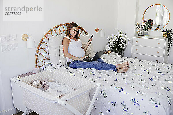 Schwangere Freiberuflerin nutzt Laptop im Bett im Heimbüro