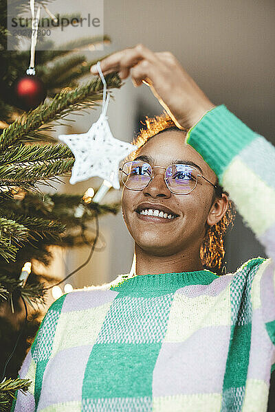 Lächelnde Frau hängt Stern am Weihnachtsbaum