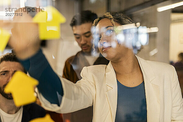 Junge Geschäftsfrau klebt im Büro Klebezettel auf Glas