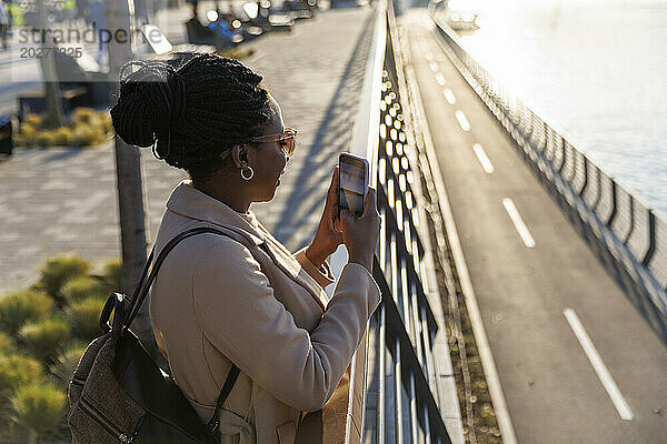 Frau fotografiert Fluss mit Smartphone bei Sonnenuntergang