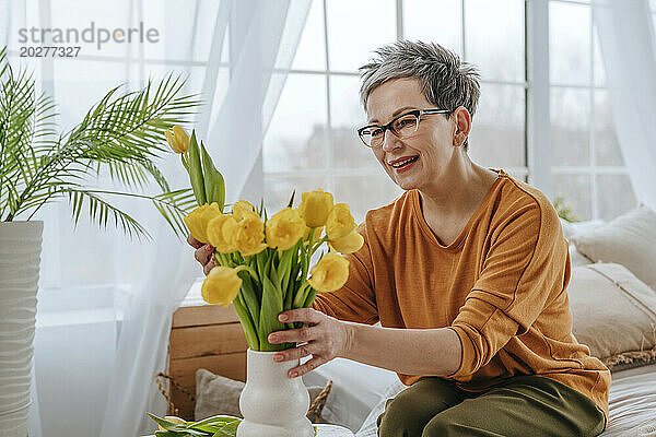 Lächelnde Frau stellt zu Hause Tulpen in eine Vase