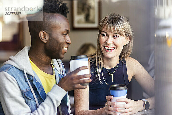 Lächelnde blonde Frau trinkt Kaffee mit einer Freundin im Café