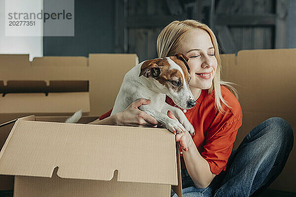 Lächelnde Frau umarmt Hund neben Kartons zu Hause