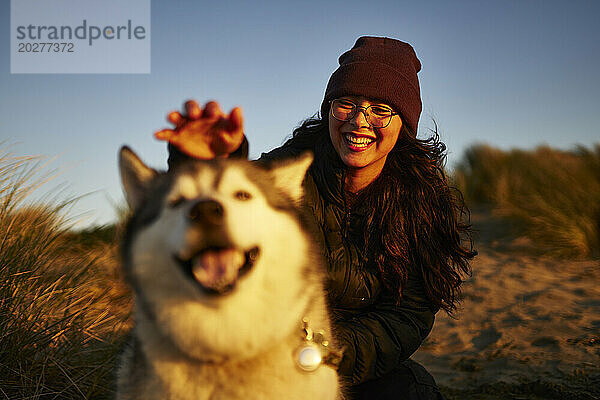 Cheerful young woman having fun with dog at sunset