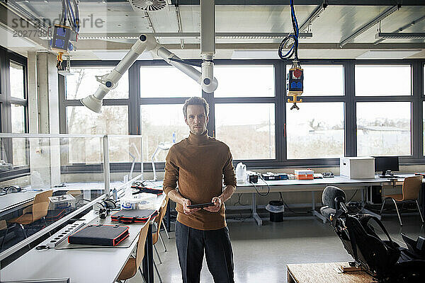 Selbstbewusster Ingenieur hält Tablet-PC in der Werkstatt