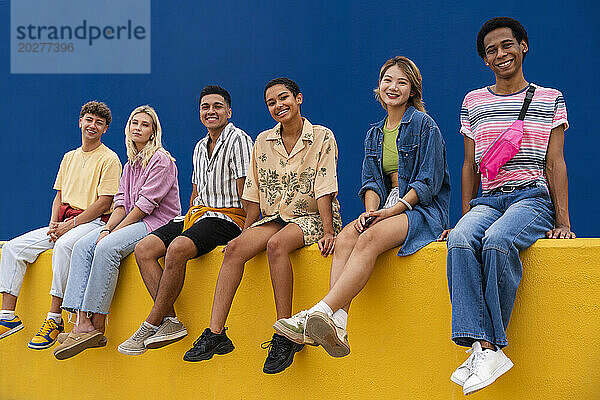 Lächelnde Freunde in bunter Kleidung sitzen zusammen an einer gelben Wand