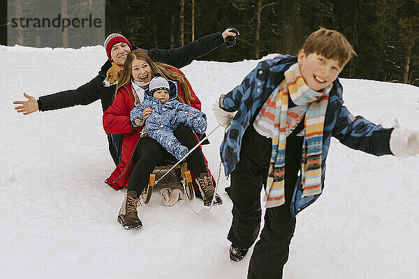Fröhlicher Junge zieht Familie auf Schlitten im Winterwald
