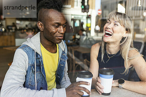 Glückliche Frau sitzt mit Freundin im Café und sieht durch Glas