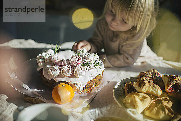 Mädchen dekoriert Kuchen auf Esstisch zu Hause