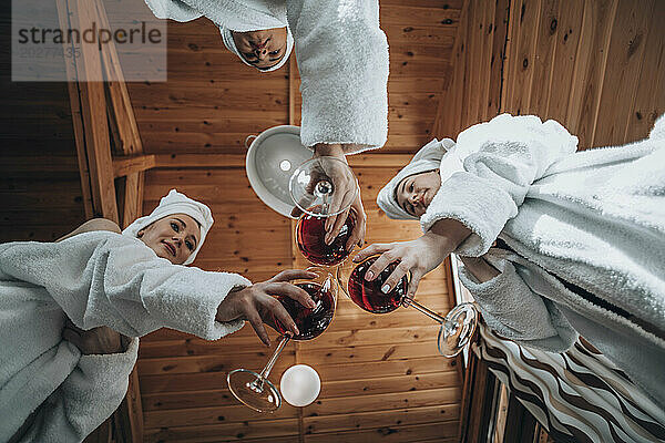 Freunde tragen Bademäntel und stoßen in der Sauna mit Wein an