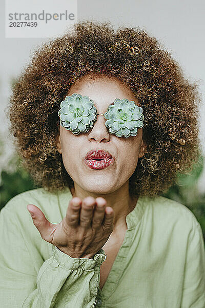 Frau trägt eine Brille mit Echeveria-Blüten und bläst einen Kuss zu