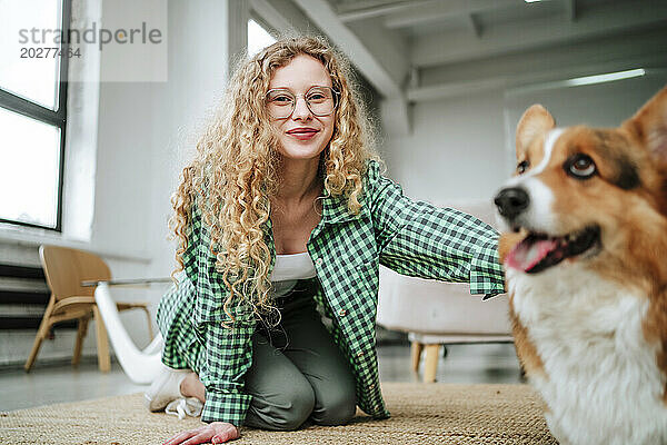 Lächelnde Frau sitzt mit Hund zu Hause auf dem Boden