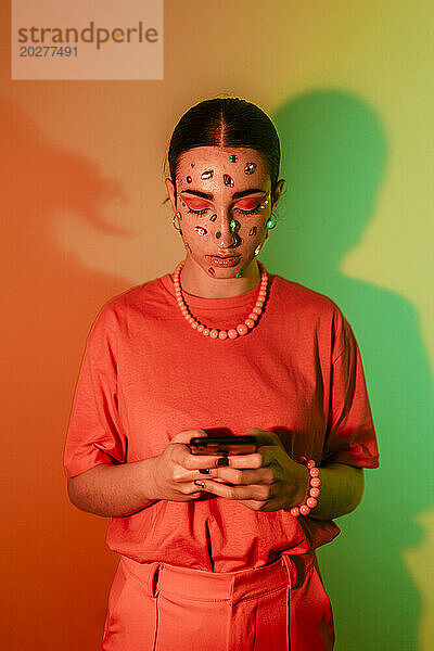 Junge Frau benutzt Smartphone vor neonfarbenem Hintergrund