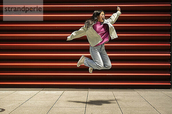Glückliche junge Frau springt vor den Fensterladen