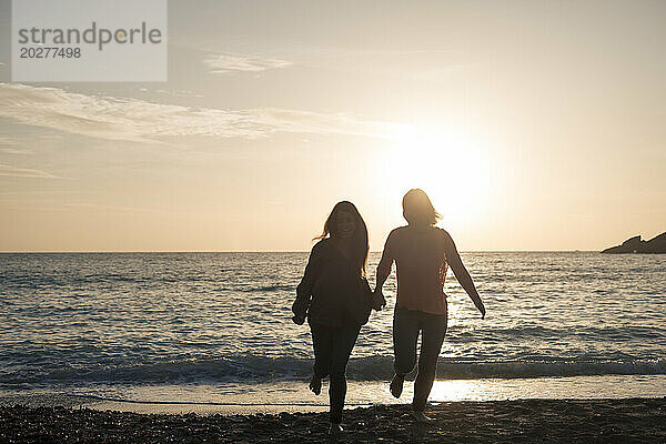 Sorglose Freunde laufen am Strand bei Sonnenuntergang am Ufer