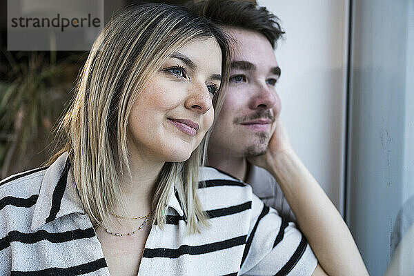 Lächelndes junges Paar  das zu Hause durch das Fenster schaut
