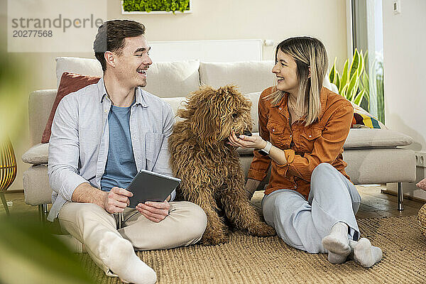Glückliches Paar sitzt mit Hund und Tablet-PC zu Hause