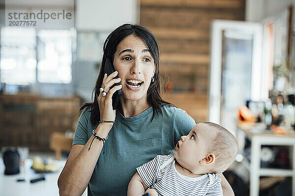 Neugieriges kleines Mädchen schaut Mutter beim Telefonieren an