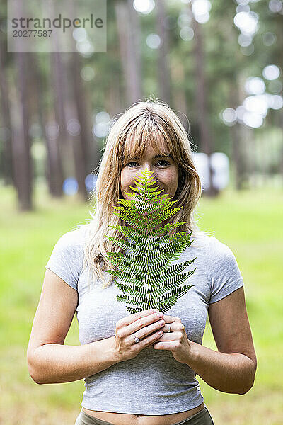 Smiling woman holding fern leaf over face